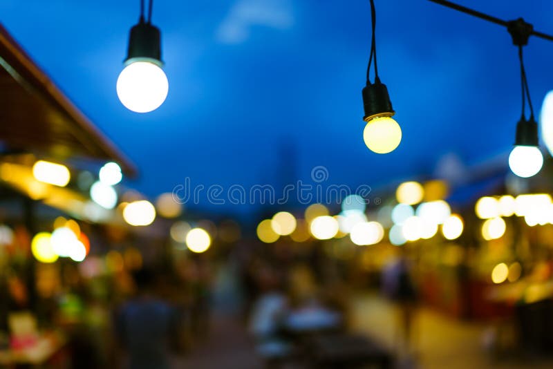Decorative outdoor string lights bulb hanging on electricity post in street night market at night time.