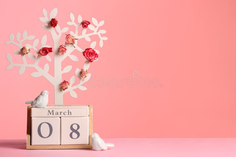 Decorative tree with flowers and wooden block calendar on table against color background. Happy Women`s Day