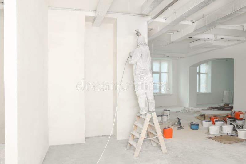 Decorator in uniform painting wall with sprayer indoors, back view royalty free stock photo