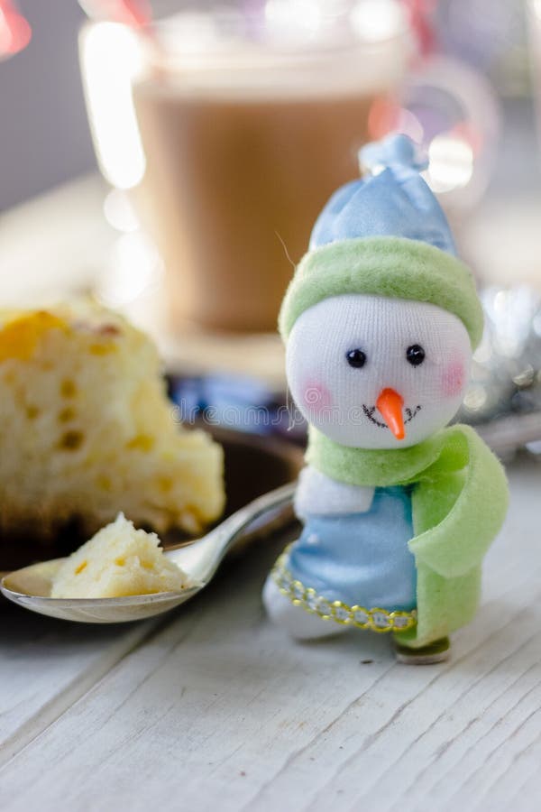 Christmas decoration at white table - snowman with piece of pie in spoon. Christmas decoration at white table - snowman with piece of pie in spoon