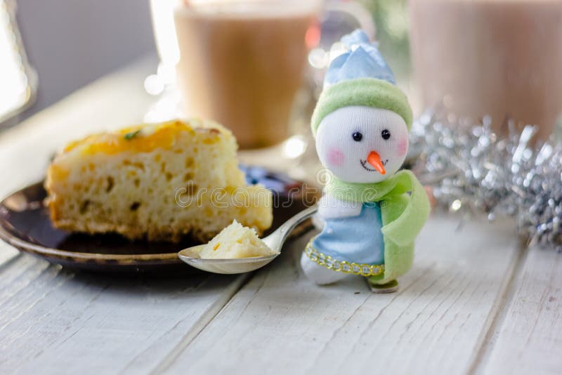 Christmas decoration at white table - snowman with piece of pie in spoon. Christmas decoration at white table - snowman with piece of pie in spoon