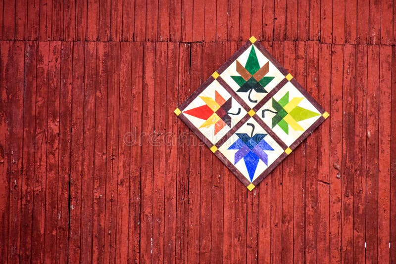 Colorful wood decoration on the side of a red barn. Details of the red painted vertical wood siding of the barn. Yellow, green, blue, orange, red, brown multi colors of the diamond shaped quilt design of leaves. Rural art and artists handmade quilt barns in Walworth County, Wisconsin. Colorful wood decoration on the side of a red barn. Details of the red painted vertical wood siding of the barn. Yellow, green, blue, orange, red, brown multi colors of the diamond shaped quilt design of leaves. Rural art and artists handmade quilt barns in Walworth County, Wisconsin.