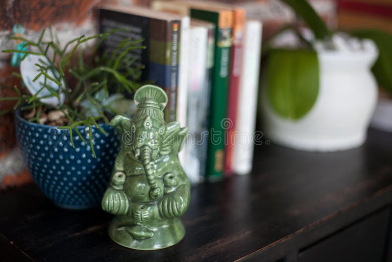 Decoração interior home, uma estatueta cerâmica de Ganesh, livros e potenciômetros de flor com as plantas na cômoda de madeira pr imagens de stock Decoração interior home, uma estatueta cerâmica de Ganesh, livros e potenciômetros de flor com as plantas na cômoda de madeira pr imagens de stock