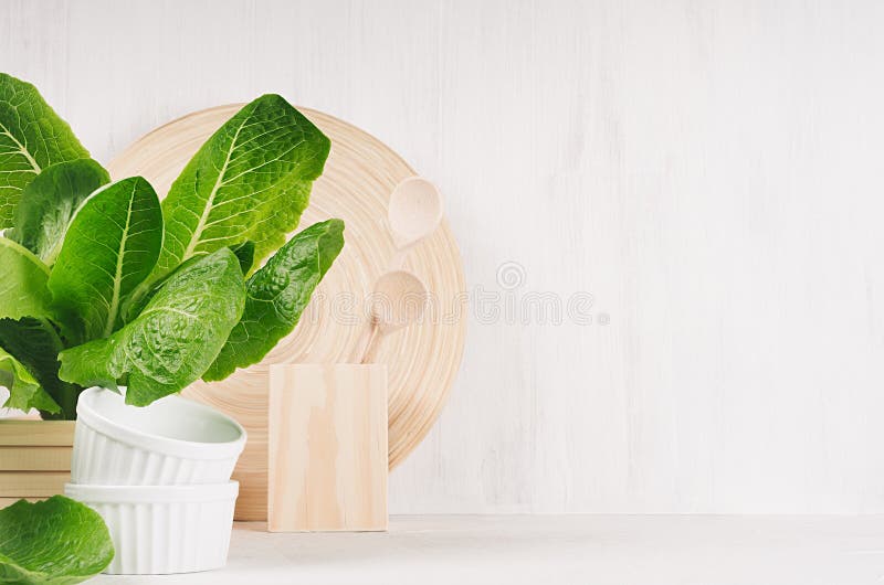 Decoração moderna branca da cozinha com o prato de madeira natural bege, utensílios, planta verde no fundo de madeira foto de stock Decoração moderna branca da cozinha com o prato de madeira natural bege, utensílios, planta verde no fundo de madeira foto de stock