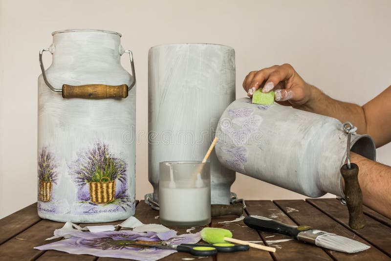 Decorating old milk churns with lavender pattern - decoupage accessories brush, scissors, tissues, sponge, paint and hands of an artist on a table. Decorating old milk churns with lavender pattern - decoupage accessories brush, scissors, tissues, sponge, paint and hands of an artist on a table.