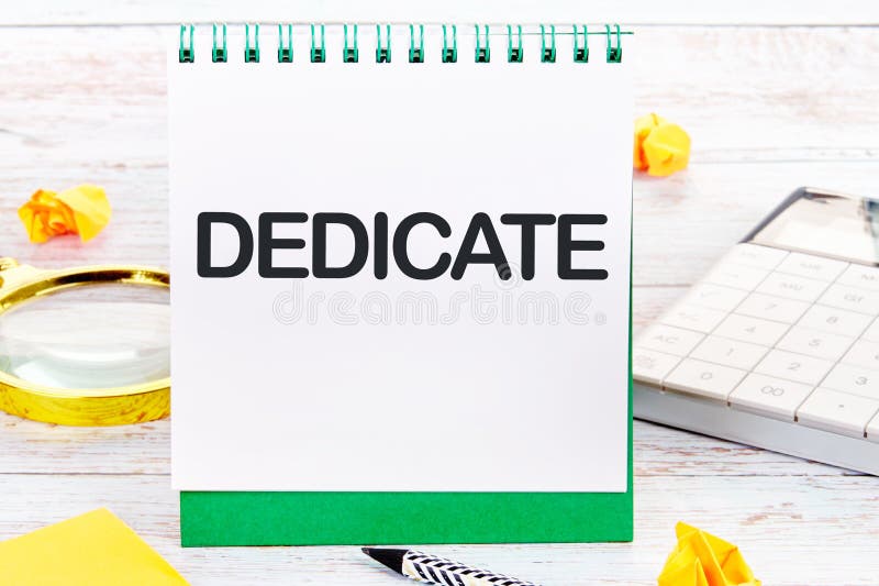 DEDICATE word written on a blank sheet of a desktop notebook stock images