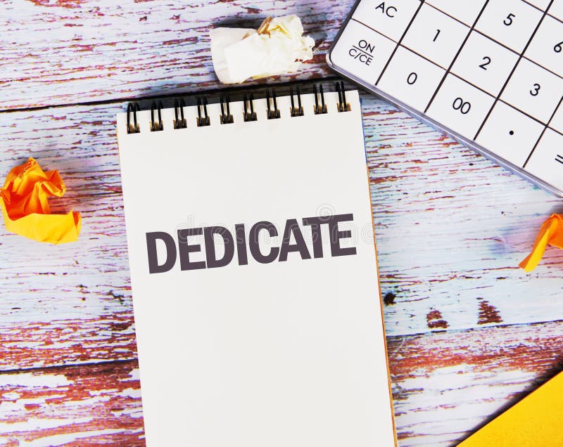 DEDICATE word written in a notebook on old boards with a calculator in the composition stock photography