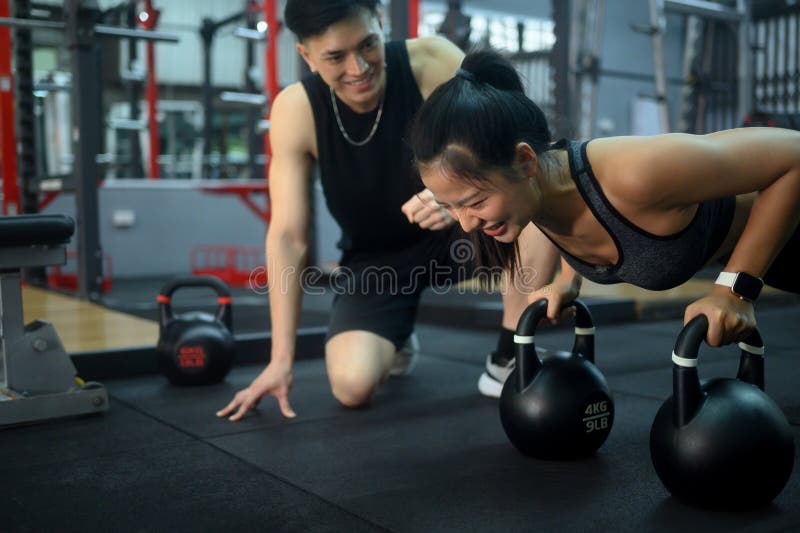 Dedikerad tränare som leder klienten genom att trycka upp kettlebell i gymmet royaltyfri bild