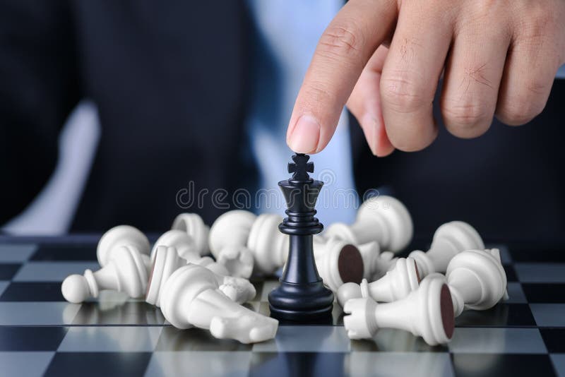 Empresário com os dedos nas mãos com a equipe atrás, sentado e movendo o rei  do xadrez para a posição de sucesso