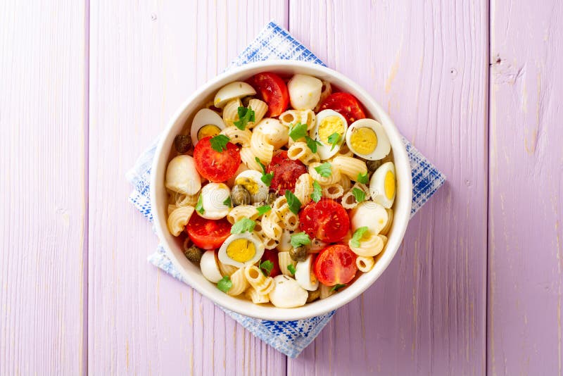 Deegwarensalade met kwartelseieren, mozarella, kersentomaten en kappertjes in kom op purpere houten achtergrond royalty-vrije stock afbeeldingen Deegwarensalade met kwartelseieren, mozarella, kersentomaten en kappertjes in kom op purpere houten achtergrond royalty-vrije stock afbeeldingen