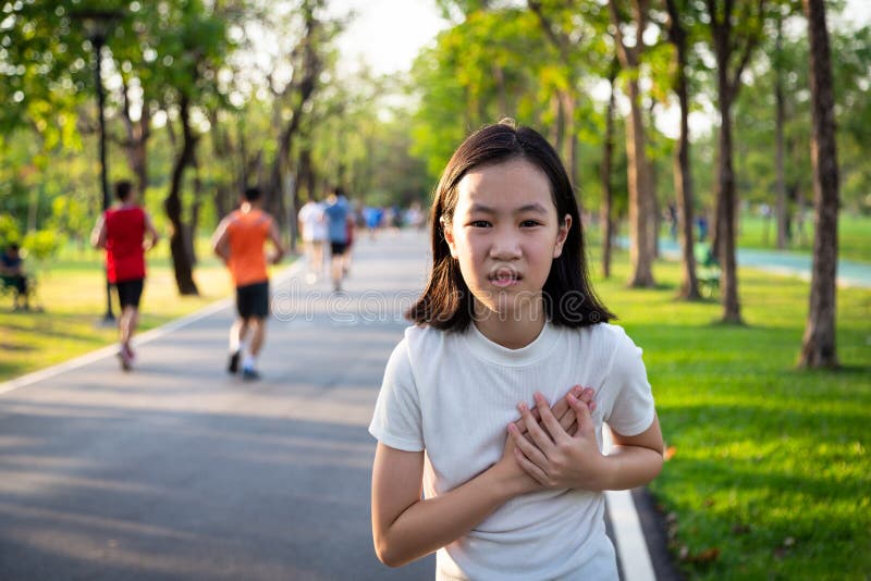 Communicates the symptoms of heart disease,immediately,Asian little girl with chest pain suffering from heart attack after run,exercise in outdoor park, cute child with symptoms difficulty breathing. Communicates the symptoms of heart disease,immediately,Asian little girl with chest pain suffering from heart attack after run,exercise in outdoor park, cute child with symptoms difficulty breathing