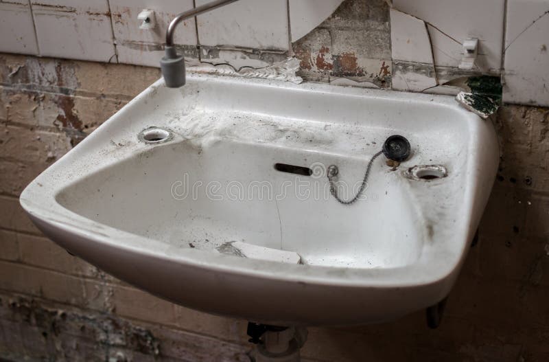 Broken and vandalized industrial factory bathroom sink with ripped piping and cracked tiling and missing taps. Broken and vandalized industrial factory bathroom sink with ripped piping and cracked tiling and missing taps