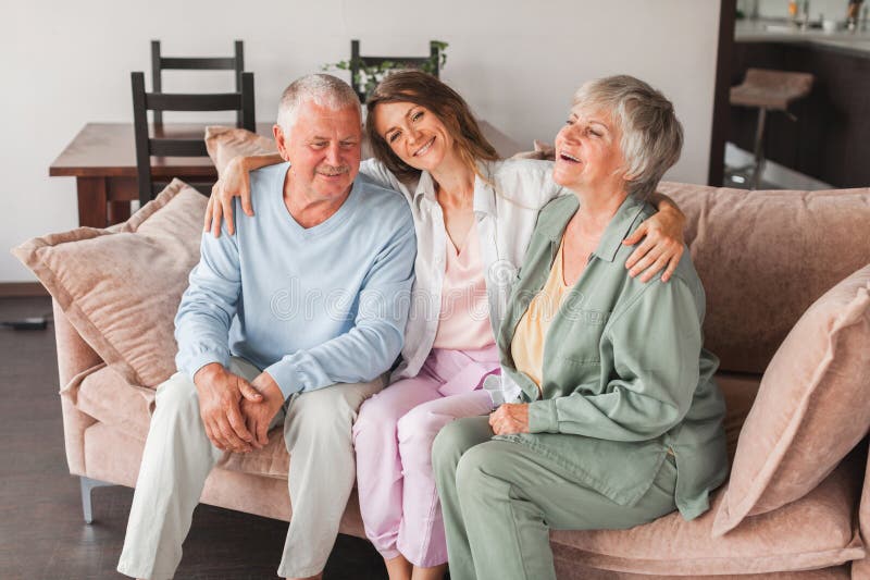 Happy defferent generation family hugging sit on sofa enjoy time together at home, laughing grown up daughter with dad and middle-aged mom warm relations, intergenerational relative people concept. Happy defferent generation family hugging sit on sofa enjoy time together at home, laughing grown up daughter with dad and middle-aged mom warm relations, intergenerational relative people concept