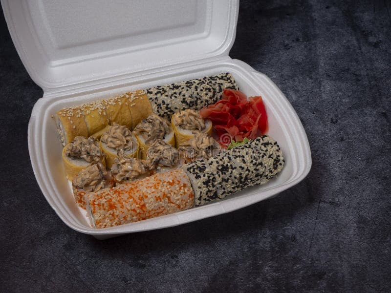 Defferent type of rolls or sushi set in a white plastic take-away box on gray stone table.