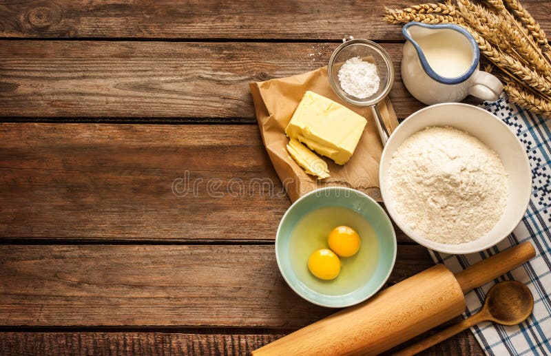 Baking cake in rural kitchen - dough recipe ingredients (eggs, flour, milk, butter, sugar) and rolling pin on vintage wood table from above. Baking cake in rural kitchen - dough recipe ingredients (eggs, flour, milk, butter, sugar) and rolling pin on vintage wood table from above