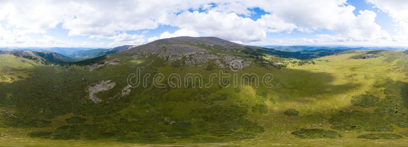 360 degree panoramic aerial view in the wild with green fields and grass and a high mountain with a rocky peak on a warm summer