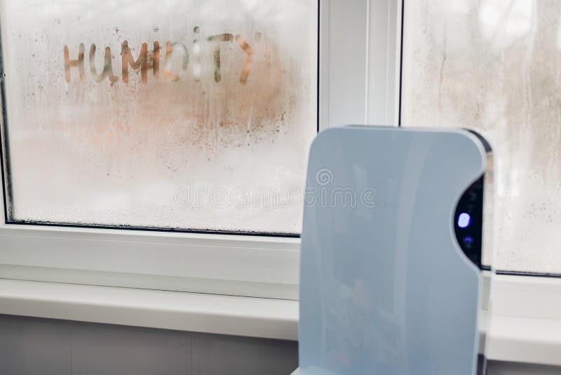 Dehumidifier with touch panel works by wet window in flat. Humidity written on window. Dampness concept