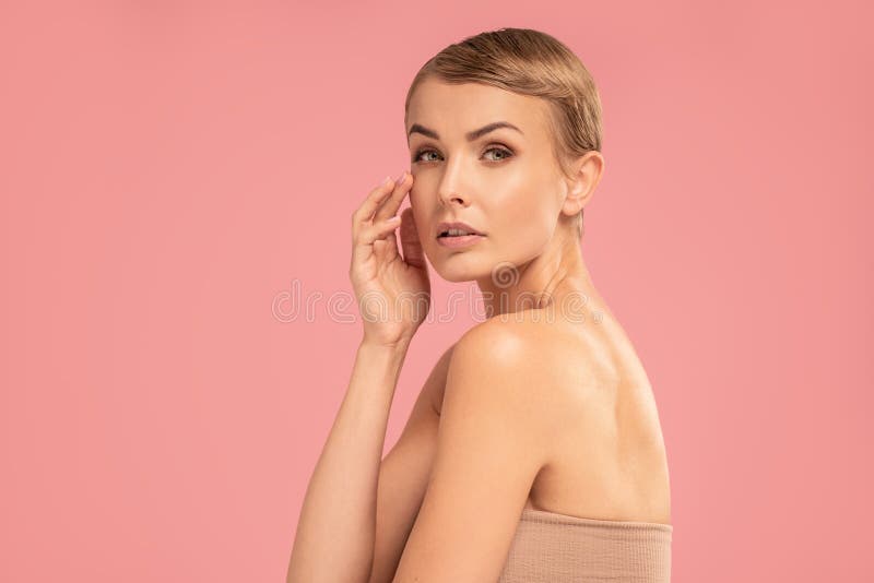 Delicate caucasian woman with blonde short hair and natural makeup looking at the camera. Beauty portrait. Studio pink pastel