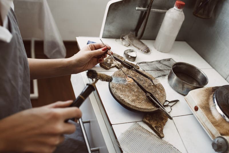 Delicate work. Side view of jeweler`s hands soldering a silver earring with flame from welding torch royalty free stock image