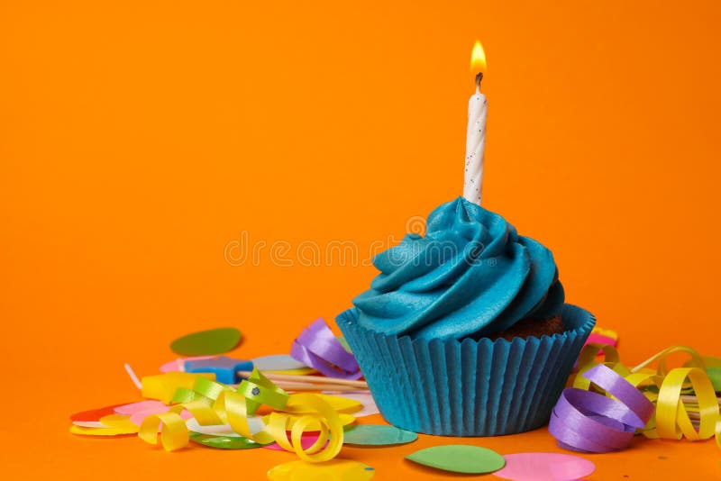 Delicious birthday cupcake with blue cream and burning candle on orange background. Delicious birthday cupcake with blue cream and burning candle on orange background