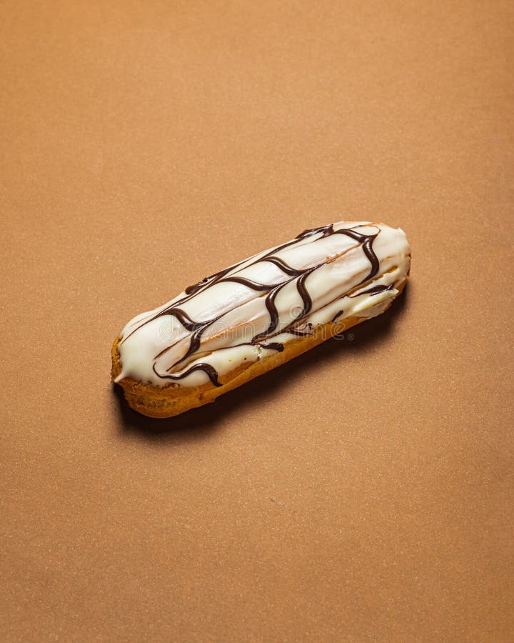 Delicioso eclair con fondant blanco y chocolate sobre fondo marrón fotos de archivo libres de regalías