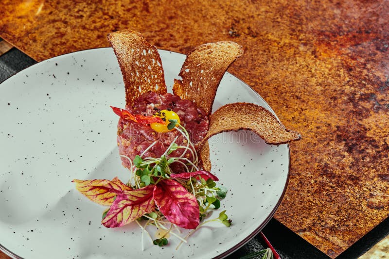 Delicioso tartar de carne con pan tostado y ensalada sobre un plato blanco sobre fondo de cobre. comida saludable hecha de fotos de archivo libres de regalías