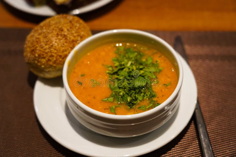 A Delicious Bowl of Lentil Soup Topped with Fresh Herbs Accompanied by a Soft Bread Roll on a Cozy Dining Setting stock photos