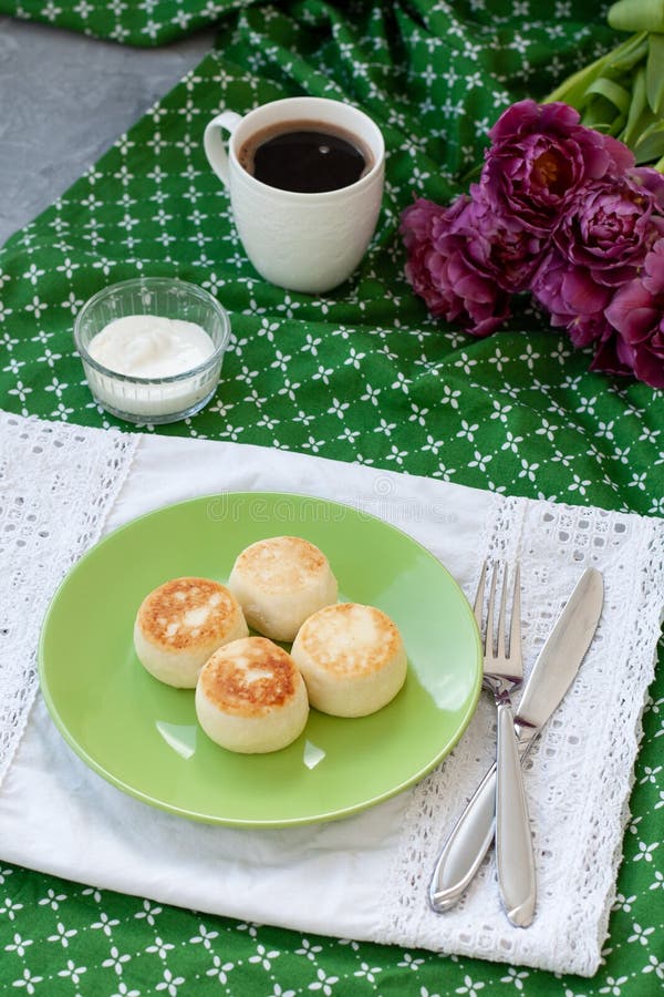 Delicious Dietary Cheesecakes from Homemade Farmer`s Cheese for breakfast, black coffee and a bouquet of purple tulips on a green stock photography Delicious Dietary Cheesecakes from Homemade Farmer`s Cheese for breakfast, black coffee and a bouquet of purple tulips on a green stock photography