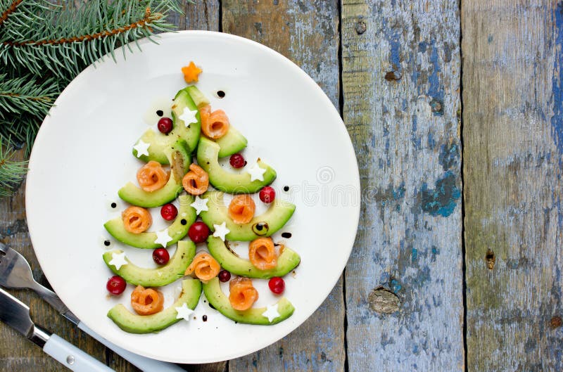 Delicious edible Christmas tree from avocado slices, salty salmon, cranberry and boiled egg stars