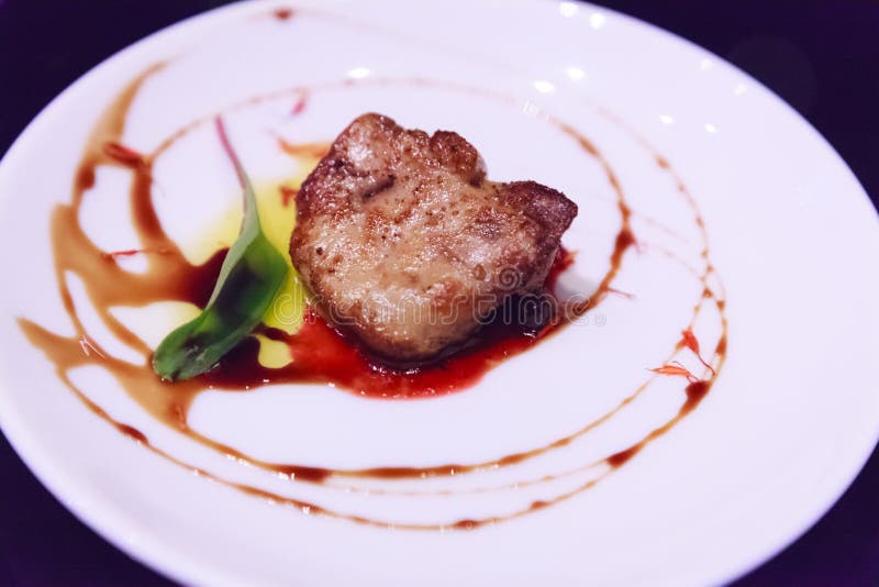 Delicious fresh sliced, pan seared Foie Gras with berry sauce decoration served on white porcelain plate. Duck or Goose Fattened