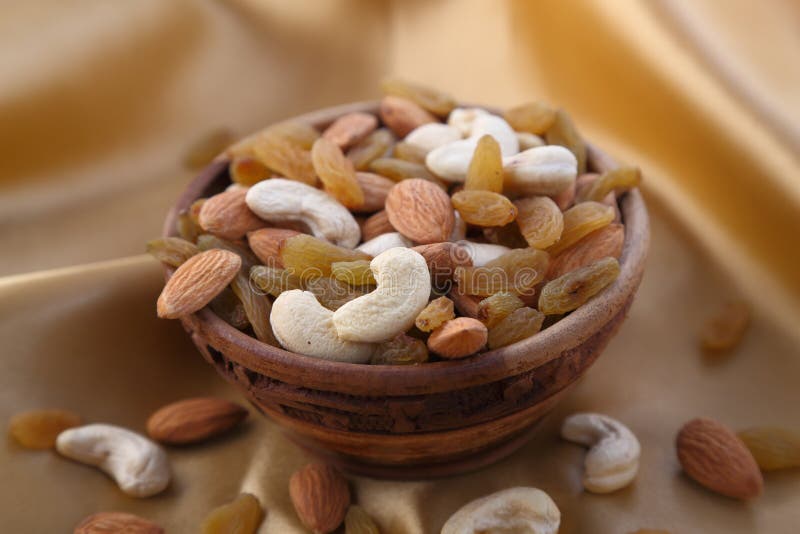 Delicious and healthy mixed dried fruit, nuts and seeds in a wooden bowl on golden silky background