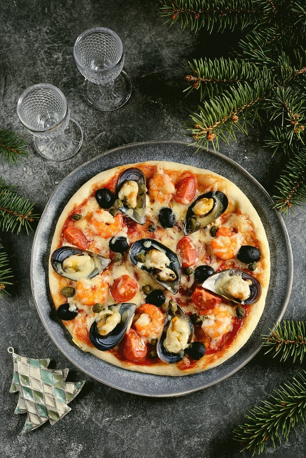 Delicious homemade pizza with seafood - mussels in shells, shrimp tails, capers and olives. Christmas background.