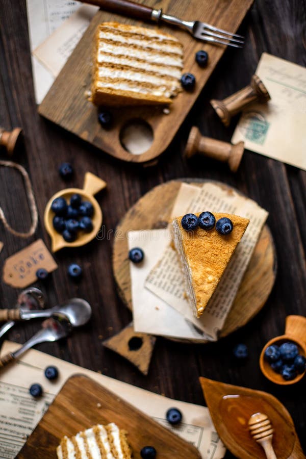 Delicious homemade slices of russian honey cake medovik with white cream, blueberries on top on wooden boards on rustic table