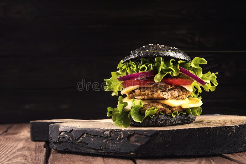 Delicious homemade vegan black burger with two chickpea cutlets, tomatoes, cheese, onion and salad on wooden table, dark