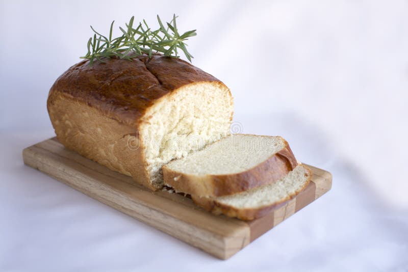 Delicious slices of homemade white bread loaf on wood cutting board with rosemary on white fabric table cloth side view. Delicious slices of homemade white bread loaf on wood cutting board with rosemary on white fabric table cloth side view