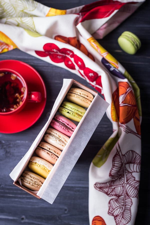 Delicious macaroons in gift box and fruit tea on dark wooden background. Top view
