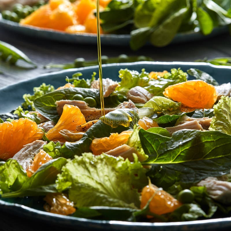 A stream of olive oil pours into the prepared salad with natural green vegetables, chicken pieces, orange slices in a royalty free stock photos A stream of olive oil pours into the prepared salad with natural green vegetables, chicken pieces, orange slices in a royalty free stock photos