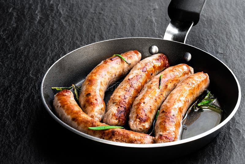 Delicious pork chipolatas sausages in a frying pan on black stone background