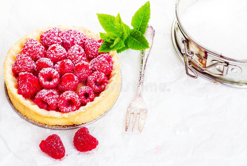 High angle view of a delicious freshly baked raspberry pie in a golden pie crust garnished with a sprig of mint and served with a silver fork. High angle view of a delicious freshly baked raspberry pie in a golden pie crust garnished with a sprig of mint and served with a silver fork