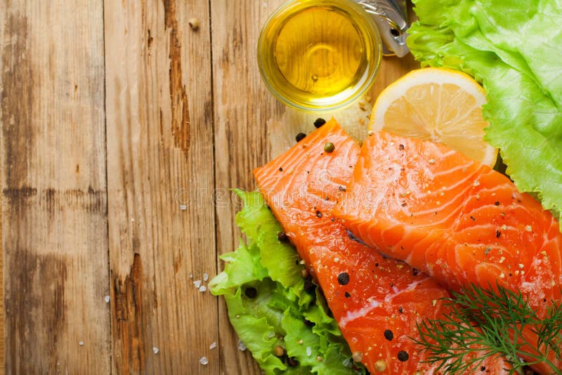 Delicious salmon fillet, rich in omega 3 oil, aromatic spices and lemon on fresh lettuce leaves on rustic wooden background. Healthy food concept. With copy space. Top view.