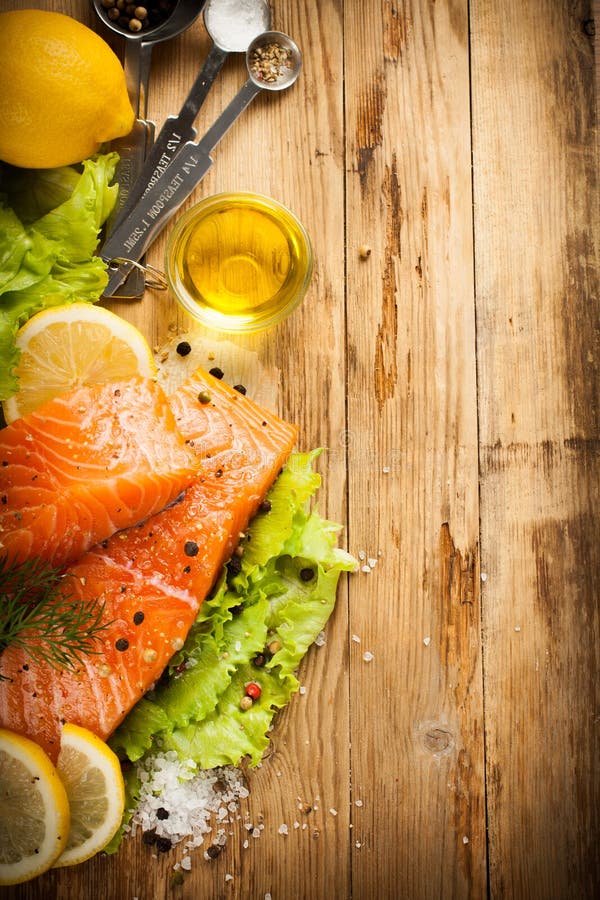 Delicious salmon fillet, rich in omega 3 oil, aromatic spices and lemon on fresh lettuce leaves on rustic wooden background. Healthy food concept. With copy space. Retro spyle toned. Top view.