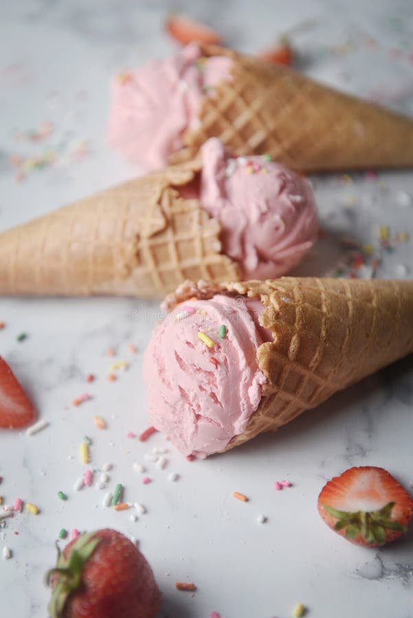 Delicious strawberry ice cream cone decorated with sugar rainbow sprinkles and fresh strawberry on marble background