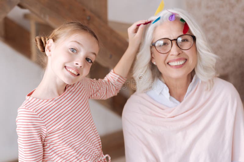 Delighted pretty girl putting a feather in her grandmothers hair