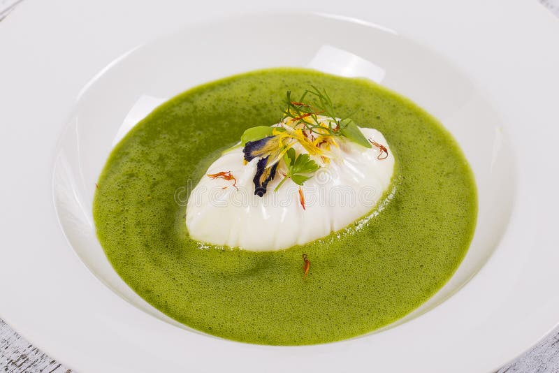 Gourmet food - poached egg and green healthy soup decorated with flowers and green leaves, close up in white plate. Gourmet food - poached egg and green healthy soup decorated with flowers and green leaves, close up in white plate