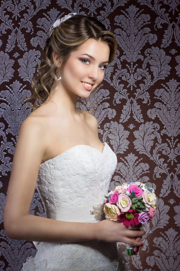 Gentle portrait of happy smiling beautiful girls in white wedding dress with a wedding bouquet in hand with beautiful hair and bright make-up, photography Studio. Gentle portrait of happy smiling beautiful girls in white wedding dress with a wedding bouquet in hand with beautiful hair and bright make-up, photography Studio