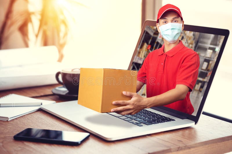 Delivery man in red shirt with hygienic mask, holding goods order in package parcel out from laptop computer with warehouse