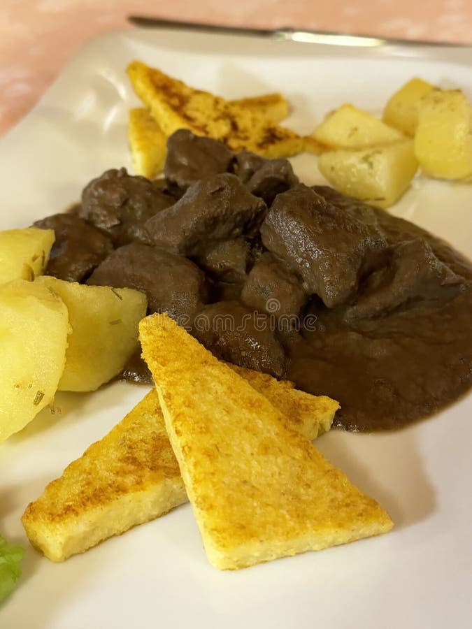 Delizioso stufato di manzo con patate e polenta grigliata su un piatto bianco immagini stock libere da diritti