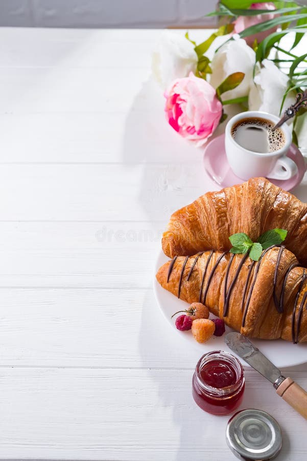 Della prima colazione croissant al forno di recente decorato con inceppamento e cioccolato, fiori sulla tavola di legno in una cu immagine stock libera da diritti Della prima colazione croissant al forno di recente decorato con inceppamento e cioccolato, fiori sulla tavola di legno in una cu immagine stock libera da diritti