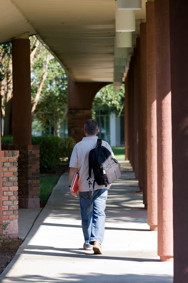 Middle aged student walks down an outdoor walkway to class on a college campus. Middle aged student walks down an outdoor walkway to class on a college campus.