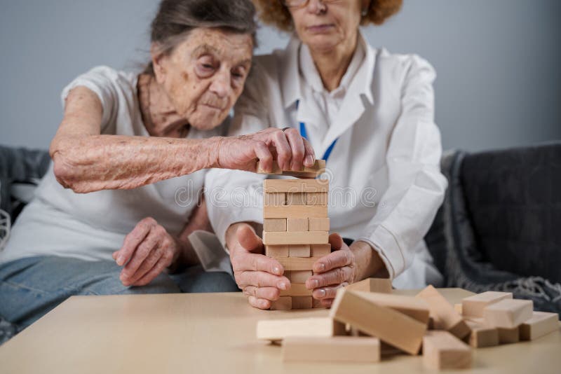 Dementia therapy in playful way, training fingers and fine motor skills, build wooden blocks into tower, playing Jenga. Senior